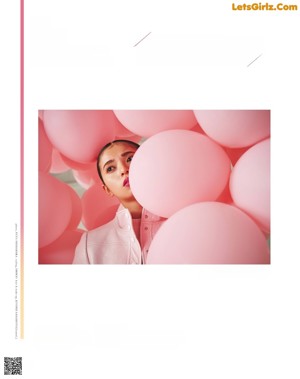 A woman in a pink jacket is surrounded by pink balloons.