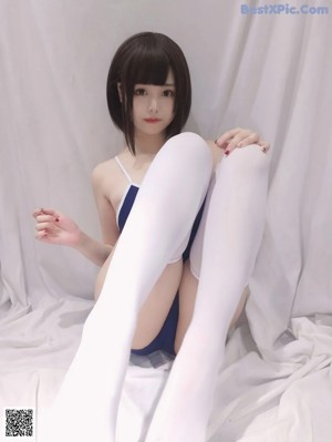 A woman in a blue bodysuit and white stockings sitting on a bed.