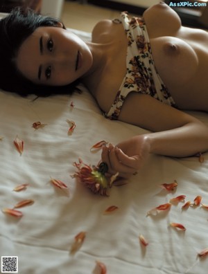 A woman laying on a bed with a flower in her mouth.