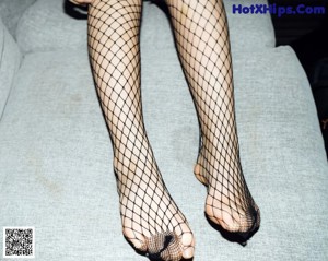 A woman in fishnet stockings posing on a couch.