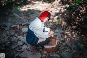 A woman in a red hooded outfit walking across a wooden bridge.