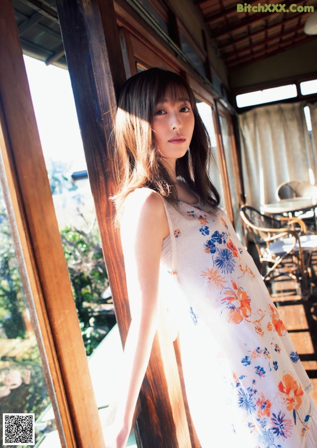 A woman in a white dress leaning against a window.