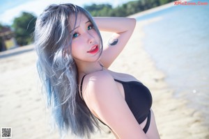 A woman in a black bikini sitting on the beach.