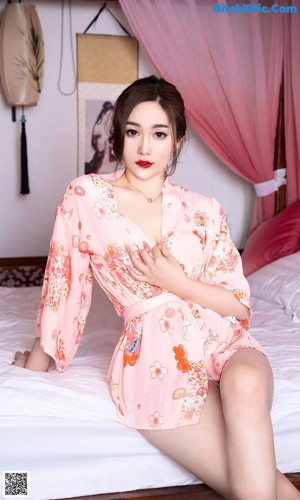 a woman in a pink robe sitting on a bed