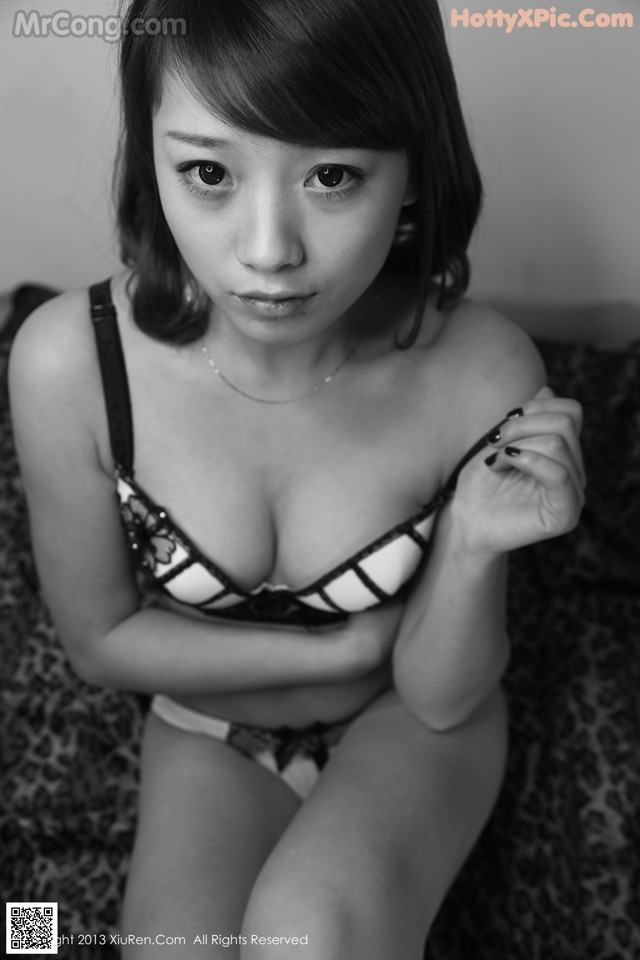 A woman in a black and white lingerie sitting on a bed.