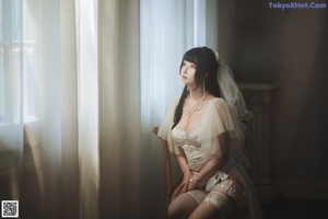 A woman in a wedding dress sitting on a chair.