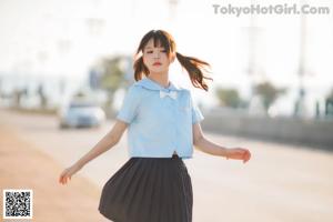 A woman in a blue shirt and black skirt is walking down the street.