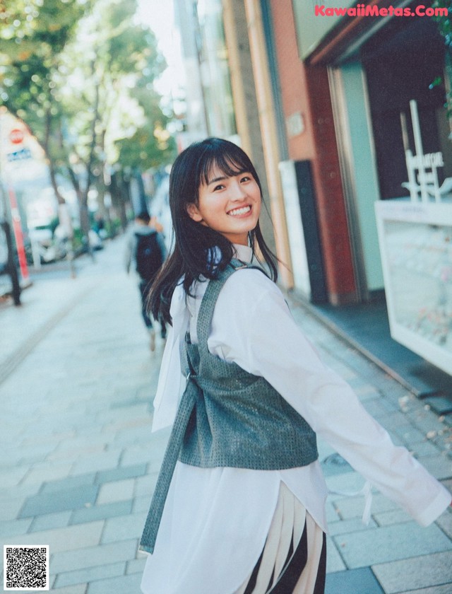 A woman walking down a sidewalk in a white shirt and black and white skirt.