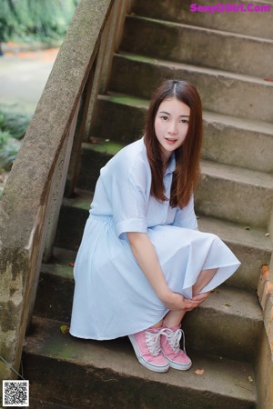 A woman in a blue and white striped dress leaning against a wall.