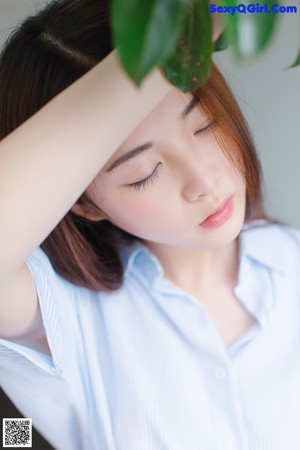 A woman in a blue and white striped shirt leaning against a bush.