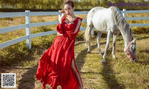 A woman in a red dress standing next to a white horse.