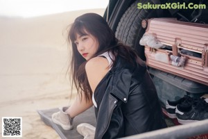 A woman sitting on top of a black car.
