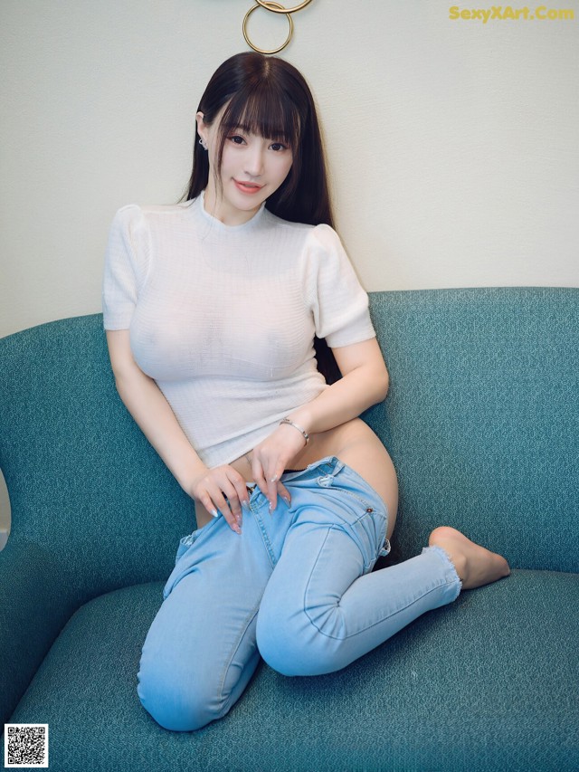 A woman sitting on a blue couch wearing a white top and jeans.